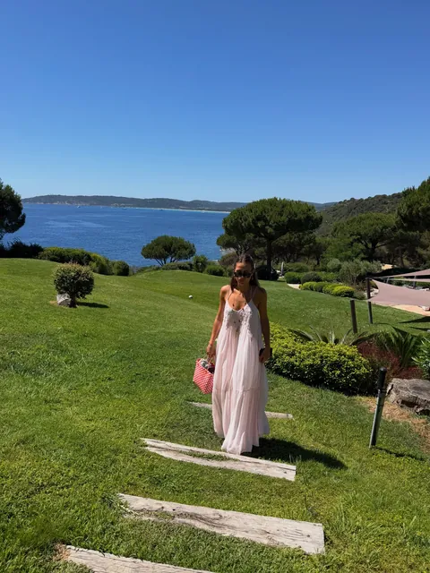Vinaya in a long pink dress on a lawn above the sea