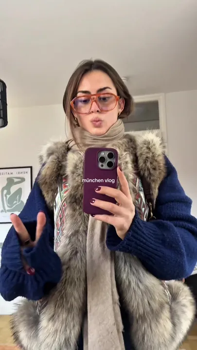 Vinaya in a fur vest filming a Munich vlog on her phone