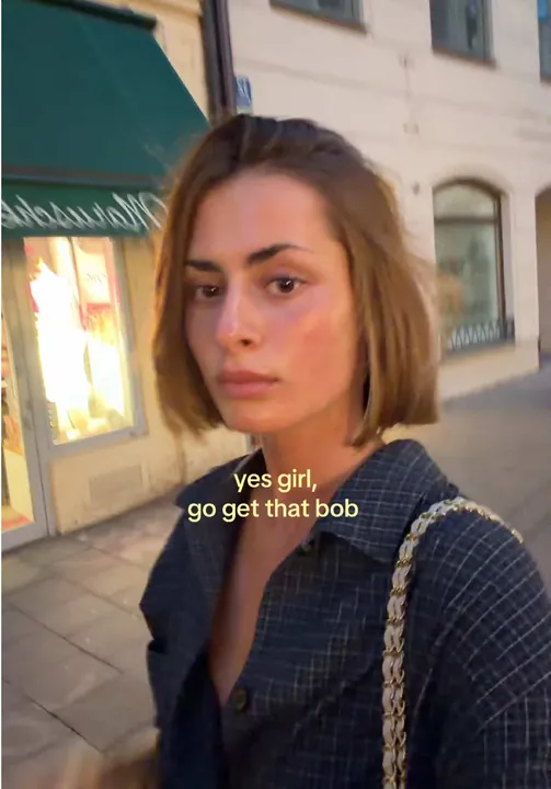 Vinaya with a fresh bob haircut in front of a shop window at dusk